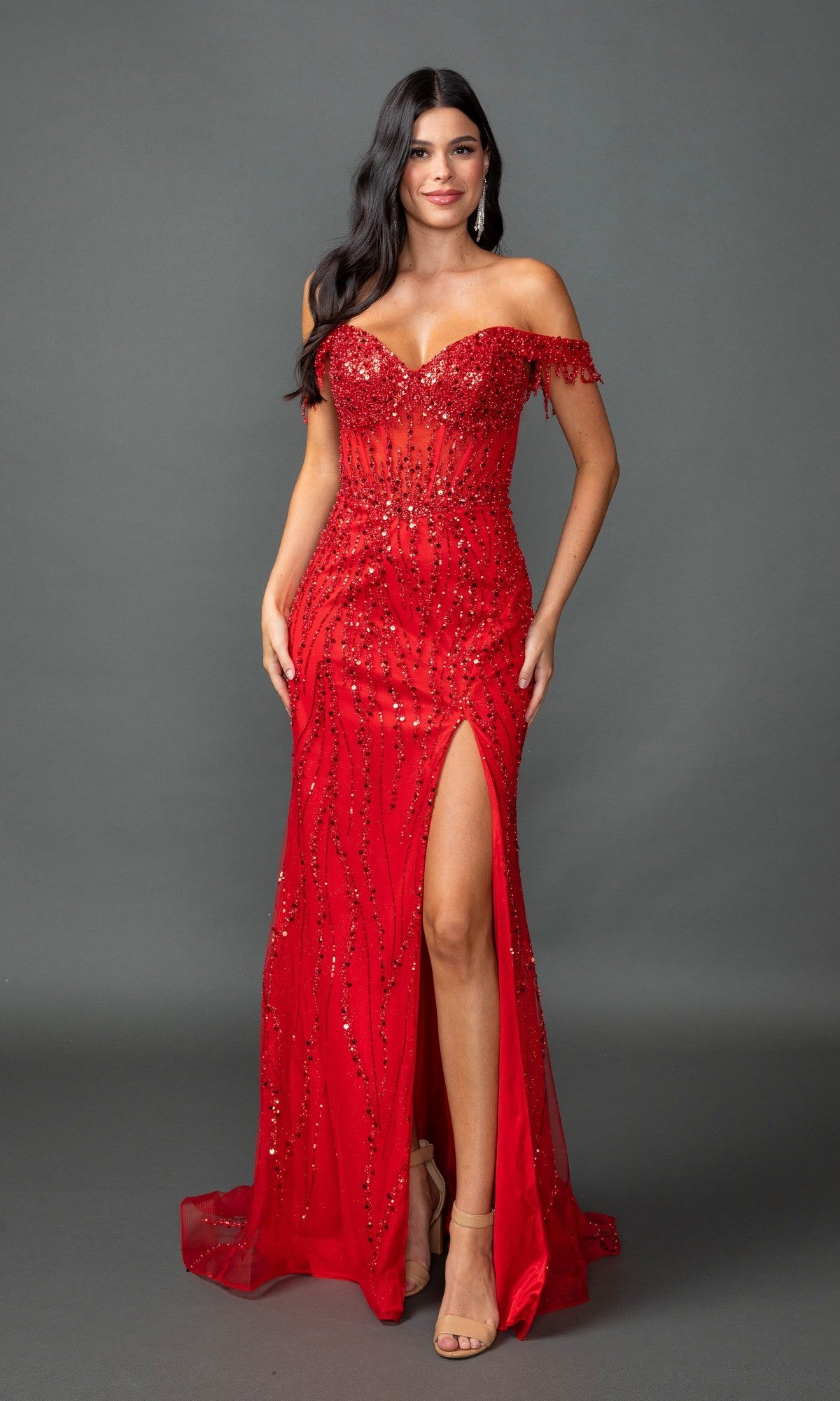 A woman poses against a gray background in the red Fringe-Strapped Long Sequin Prom Dress 4385, featuring an off-the-shoulder design, sweetheart neckline, beaded details, and a high slit.